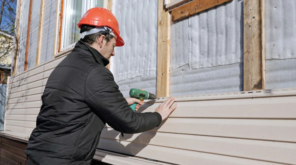 Siding replacement professional using a power drill to install new tan vinyl siding on a home exterior in Lakeland, FL